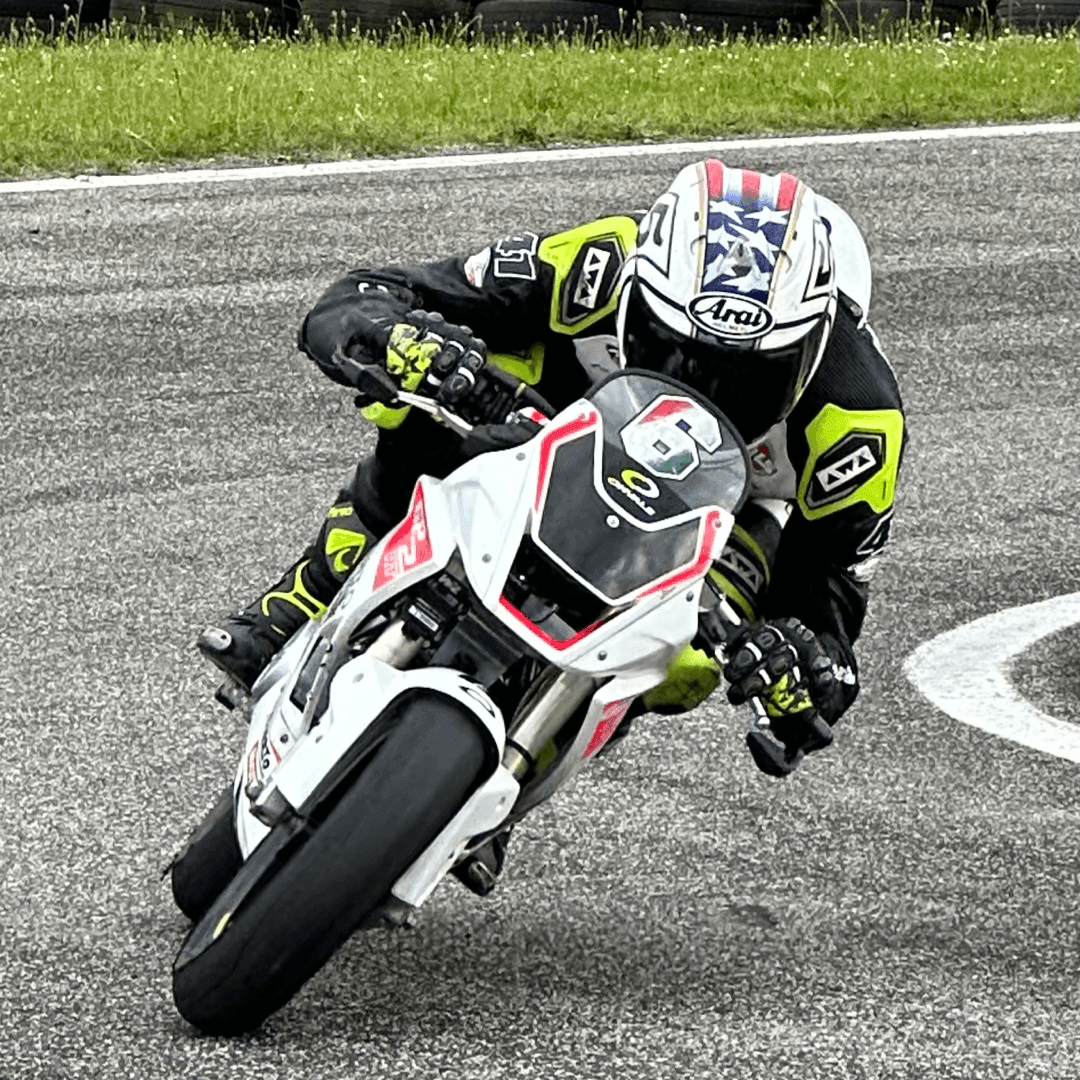 Motorcyclist in full gear and helmet leaning into a sharp turn on a racing track.