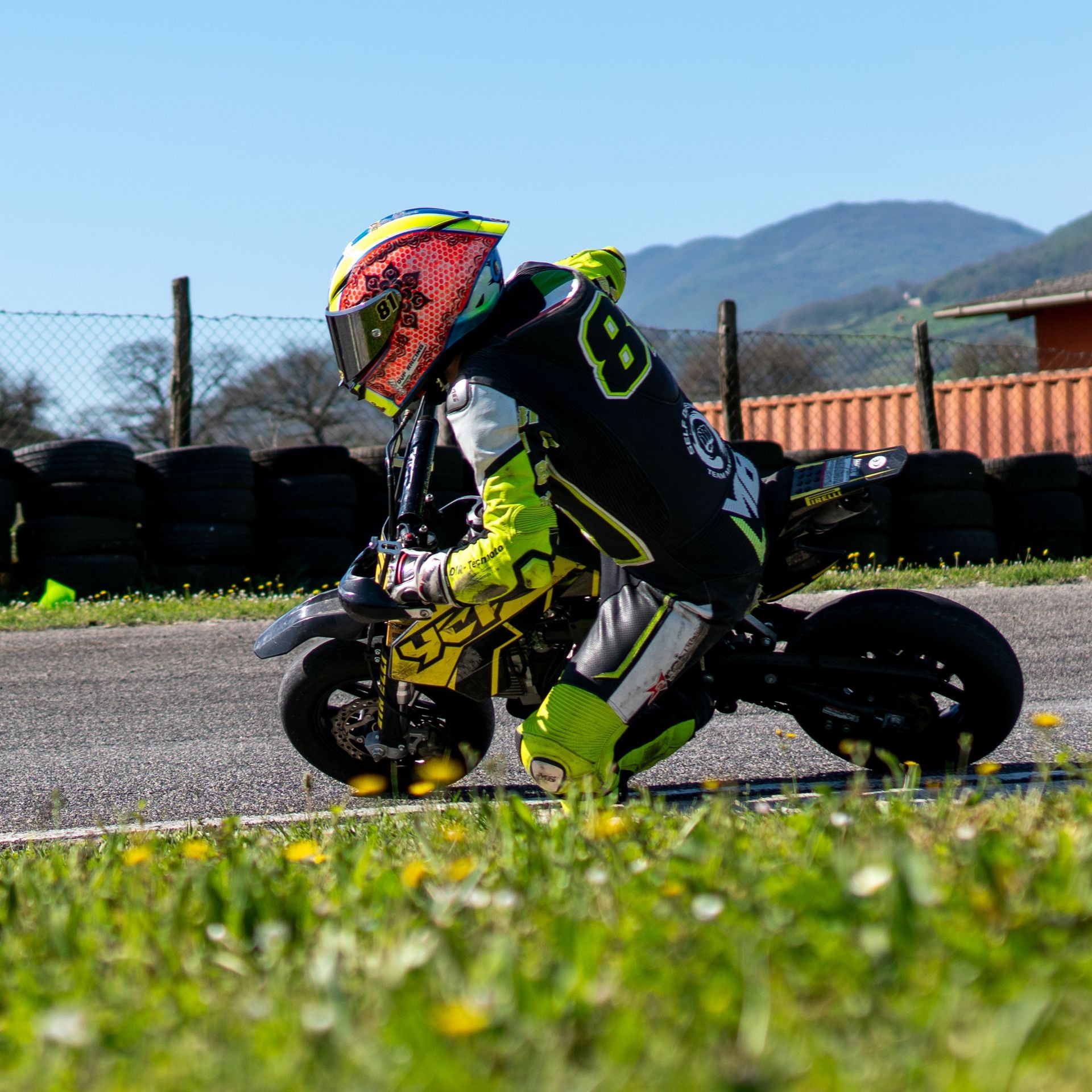 Person in racing gear riding a mini motorcycle on a track with mountainous background.