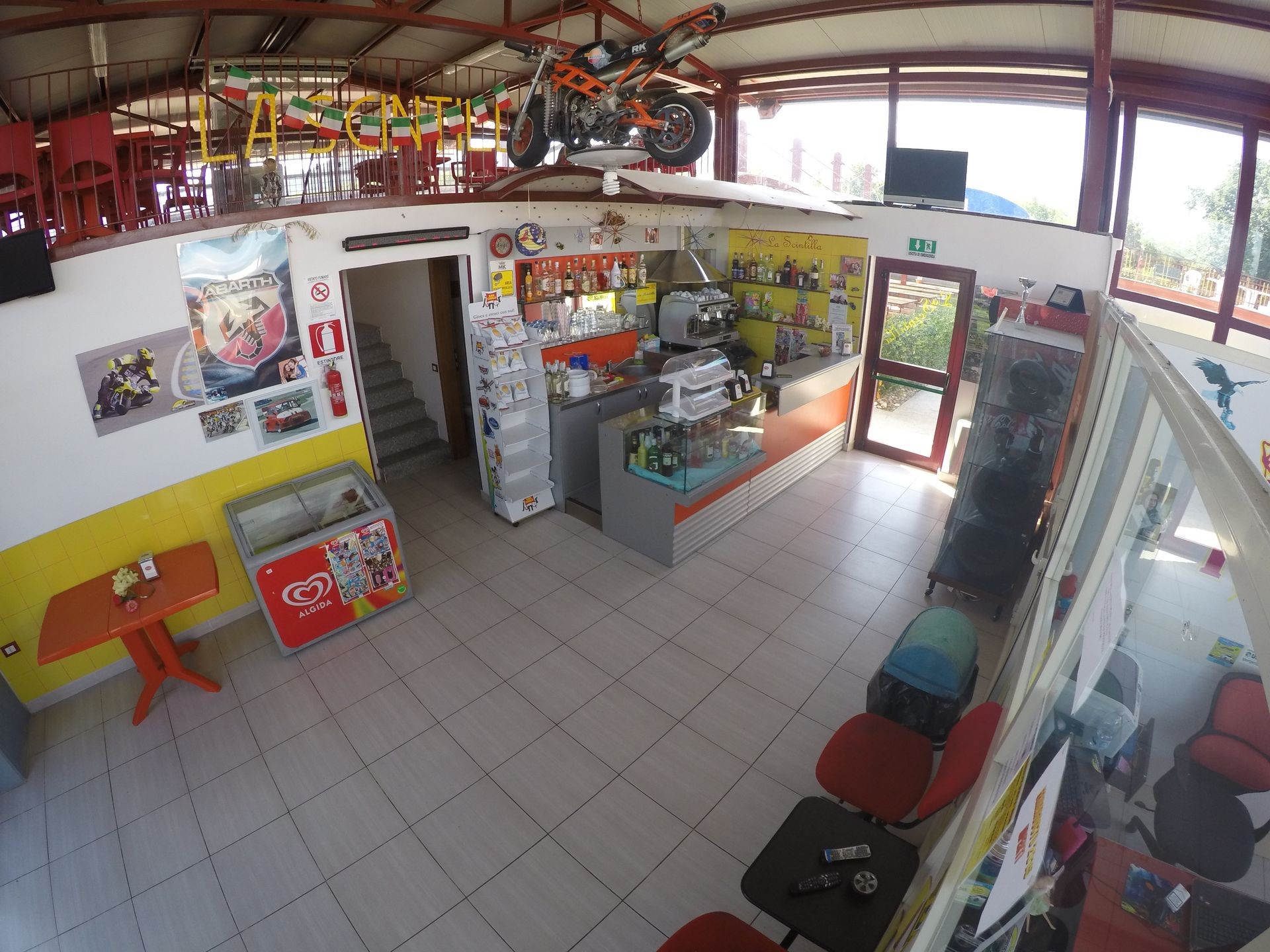 Interior of a small cafe with a staircase, motorbike decor, and posters on the walls.