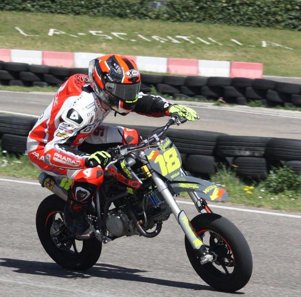 Motorcyclist in racing gear leaning into a sharp turn on a mini motorcycle at a track.