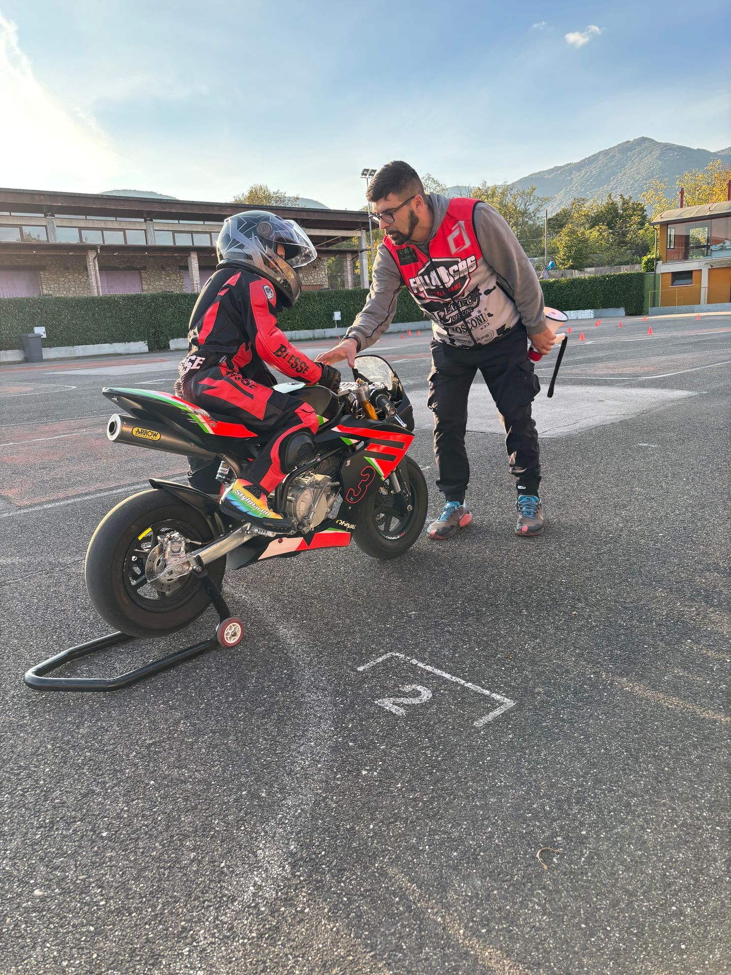 Person in racing gear on a motorcycle receiving instructions from another person on a track.